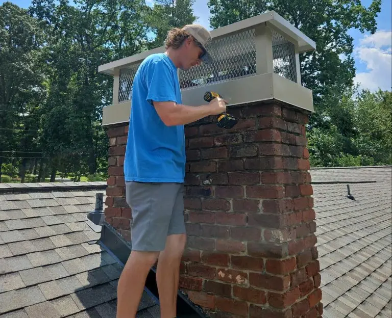 Technician installing a custom chimney cap on a red brick chimney with a power drill