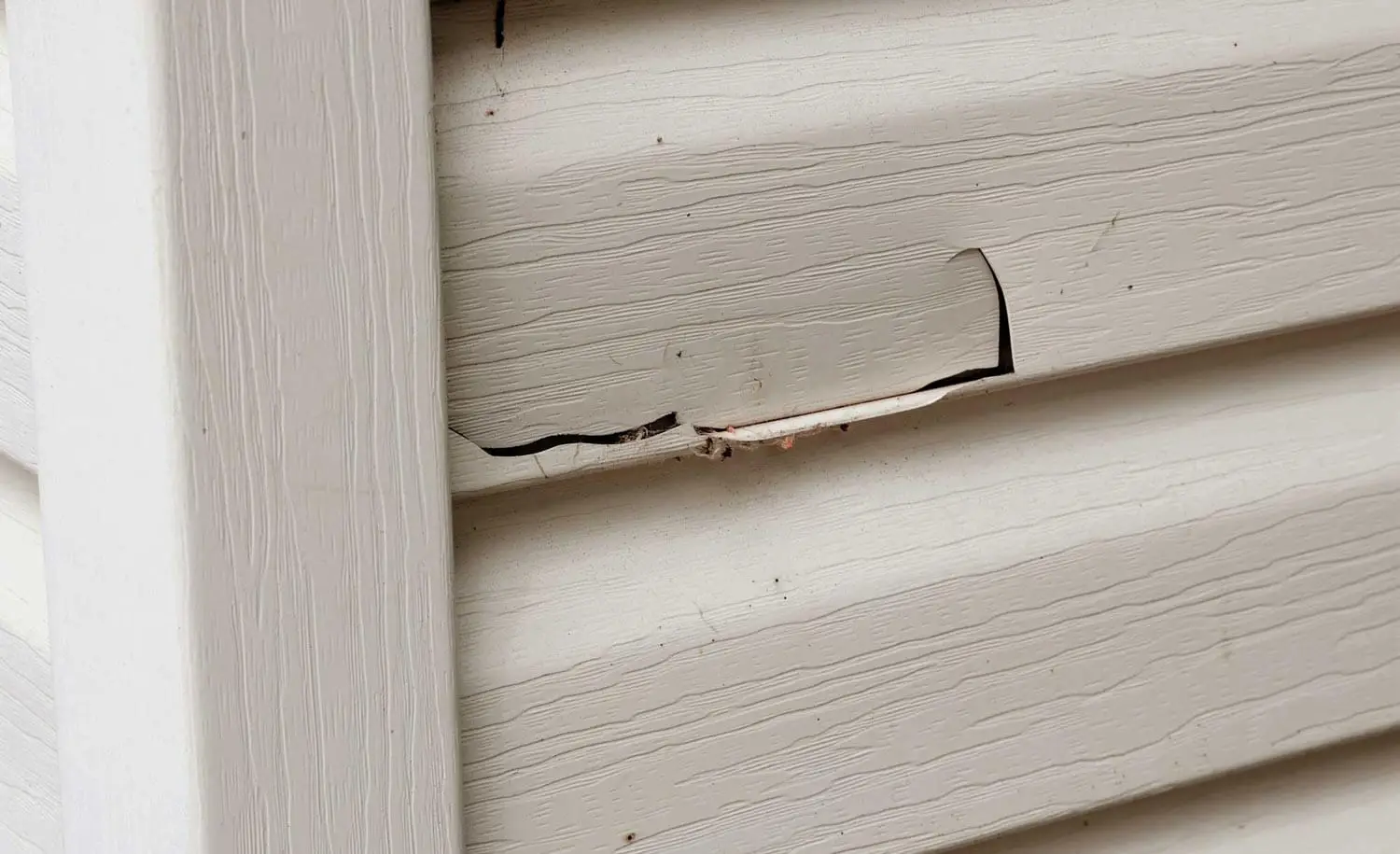 Close-up of cracked and broken beige vinyl siding on a residential home