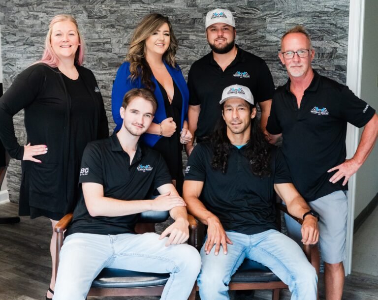 Smithrock Roofing team members posing together in the office in front of a gray stone accent wall
