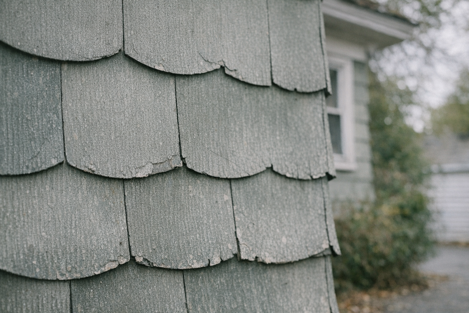 Close-up of asbestos siding shingles with scalloped edges installed in overlapping horizontal courses on an older home